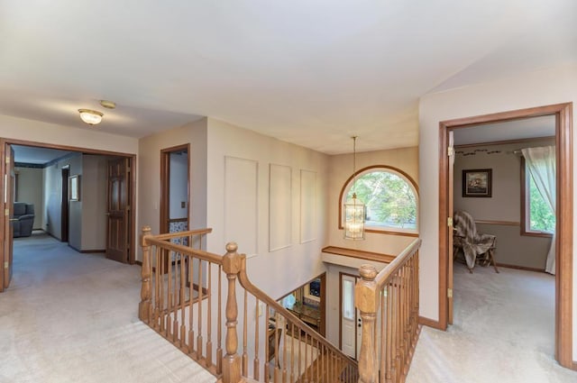 hall with an upstairs landing, light carpet, and baseboards