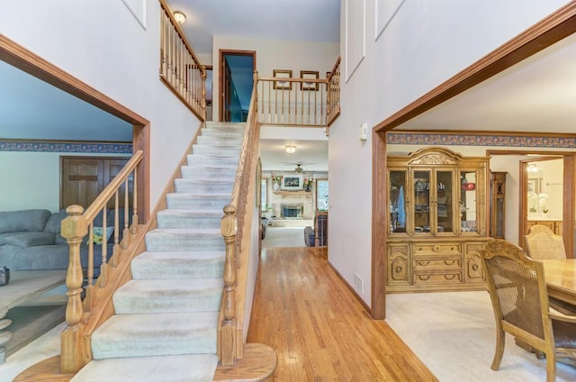 entrance foyer with stairs, ceiling fan, a fireplace, a high ceiling, and wood finished floors