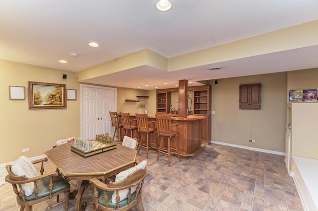dining room with bar, baseboards, stone finish flooring, and recessed lighting