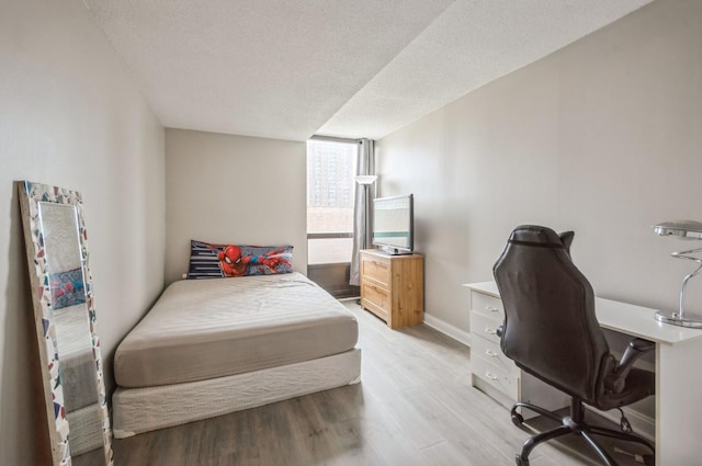 bedroom with light wood finished floors, a desk, baseboards, and a textured ceiling