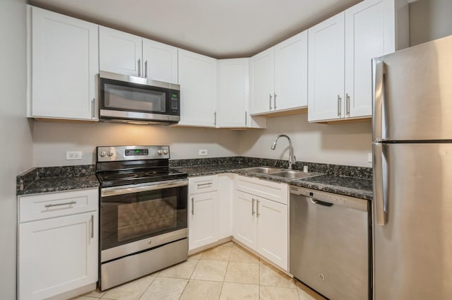 kitchen featuring stainless steel appliances, a sink, white cabinets, light tile patterned floors, and dark stone countertops