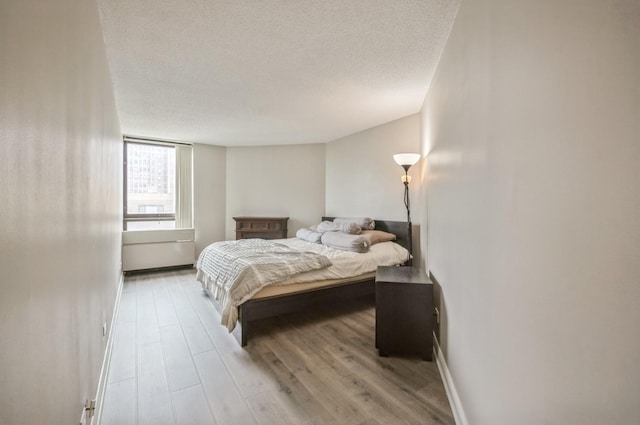 bedroom featuring wood finished floors, a textured ceiling, and baseboards