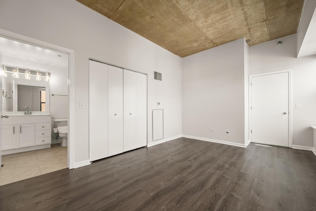 unfurnished bedroom with wood finished floors, a closet, ensuite bath, baseboards, and a sink