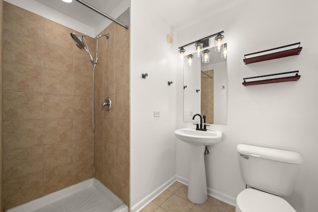 bathroom featuring toilet, tile patterned floors, a tile shower, and baseboards