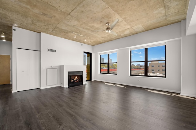 unfurnished living room with dark wood-style flooring, a ceiling fan, a lit fireplace, and baseboards
