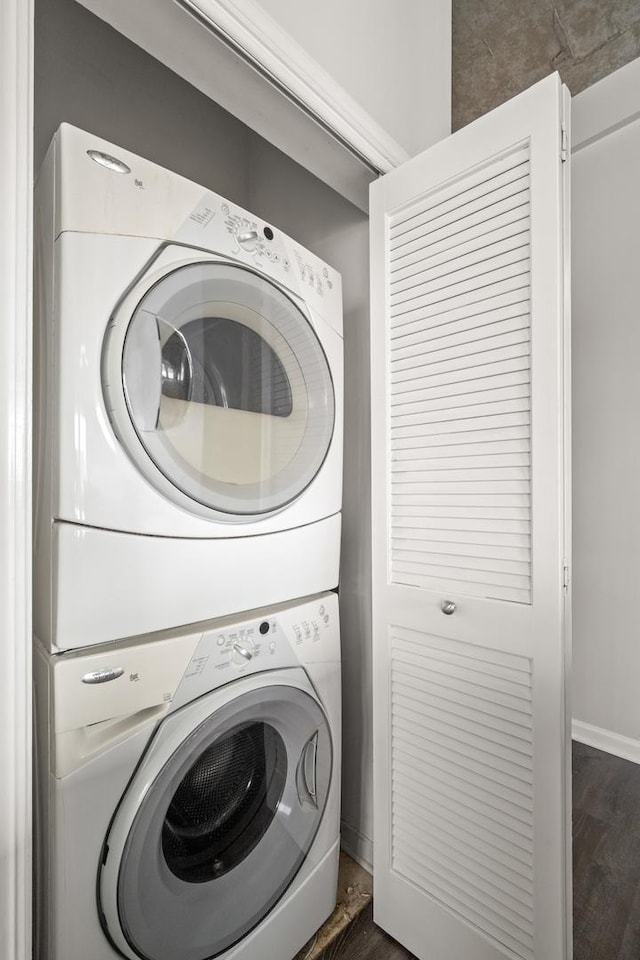 clothes washing area featuring stacked washing machine and dryer, dark wood-type flooring, and baseboards