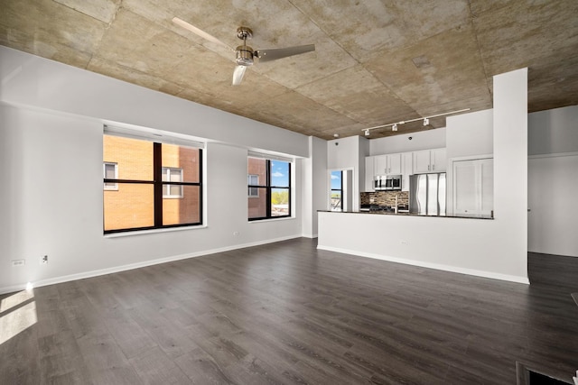 unfurnished living room featuring a ceiling fan, dark wood-style flooring, track lighting, and baseboards