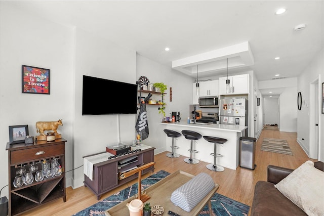 living room with light wood finished floors, a raised ceiling, recessed lighting, and baseboards
