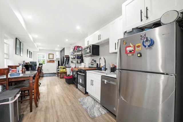 kitchen featuring stainless steel appliances, light wood-type flooring, white cabinets, a sink, and backsplash