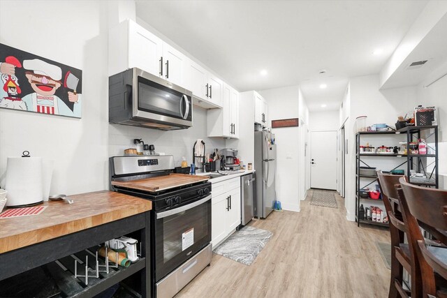 kitchen featuring appliances with stainless steel finishes, white cabinets, light wood-style floors, a sink, and wood counters