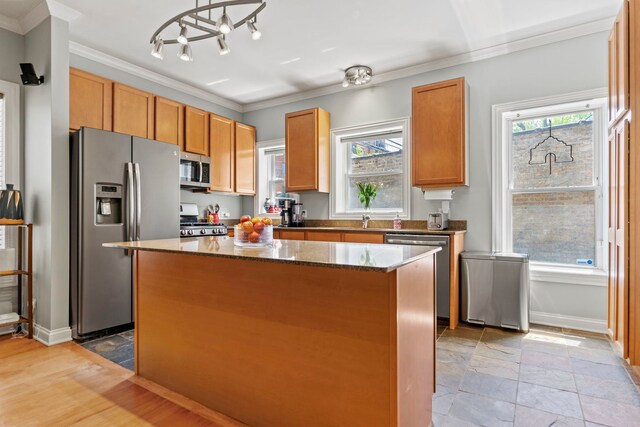 kitchen with appliances with stainless steel finishes, a center island, crown molding, baseboards, and dark stone counters