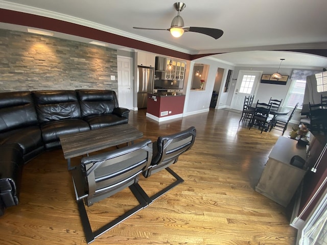 living room with a ceiling fan, crown molding, arched walkways, wood finished floors, and baseboards