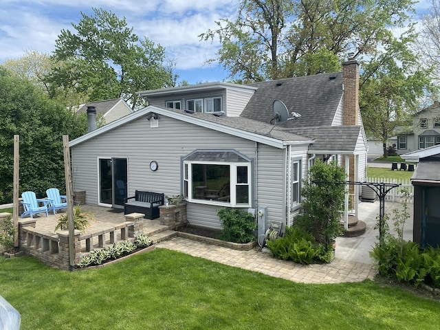rear view of property featuring a patio, a lawn, a chimney, and roof with shingles