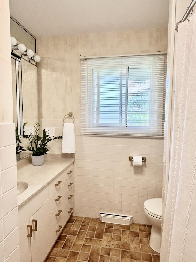 bathroom featuring toilet, vanity, a baseboard radiator, and tile walls