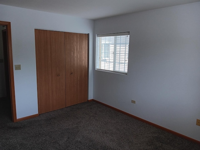 unfurnished bedroom featuring a closet, dark colored carpet, and baseboards