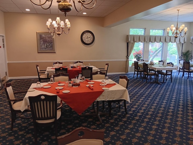 carpeted dining room featuring a chandelier, a drop ceiling, and baseboards