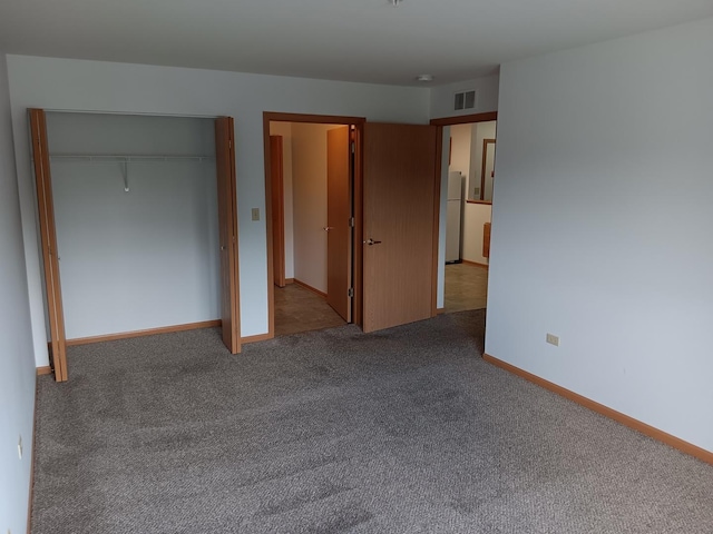 unfurnished bedroom with freestanding refrigerator, carpet flooring, a closet, and baseboards