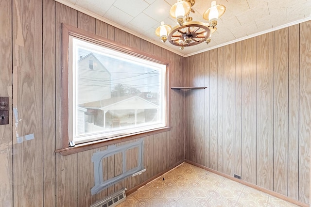 spare room with a chandelier, tile patterned floors, wood walls, and crown molding