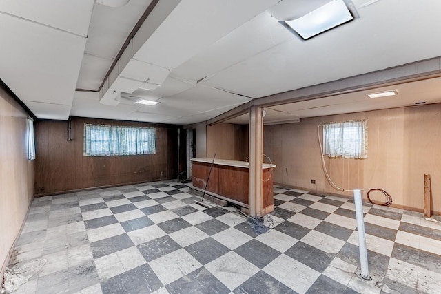 basement featuring tile patterned floors, wood walls, plenty of natural light, and a dry bar