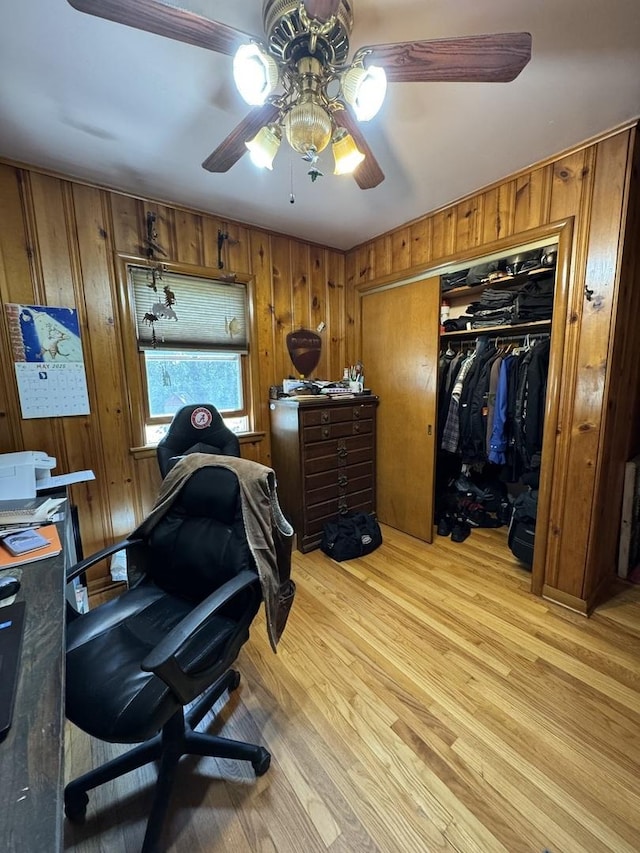 office area with a ceiling fan, light wood-style floors, and wood walls