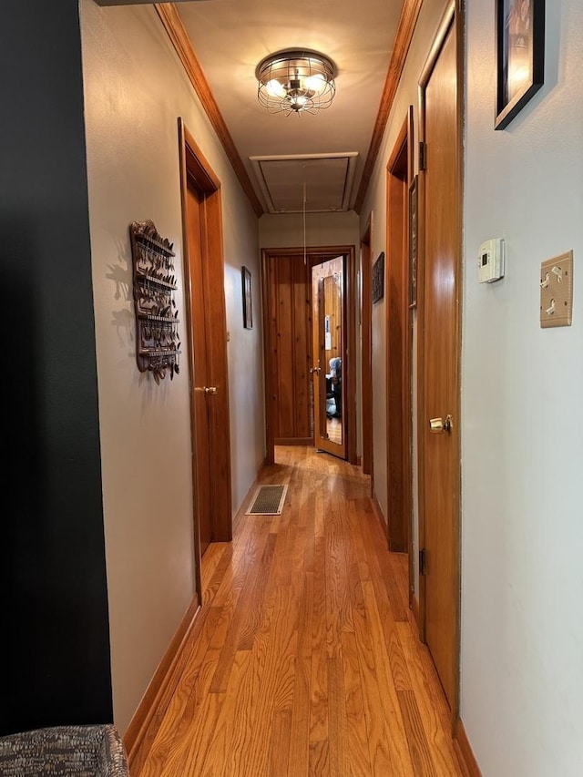 hallway featuring attic access, light wood-type flooring, and baseboards