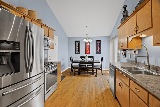 kitchen with appliances with stainless steel finishes, a sink, lofted ceiling, light wood finished floors, and a chandelier