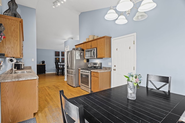 kitchen with appliances with stainless steel finishes, a sink, a chandelier, high vaulted ceiling, and light wood finished floors