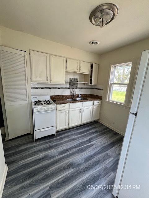 kitchen featuring white appliances, a sink, dark countertops, white cabinetry, and backsplash