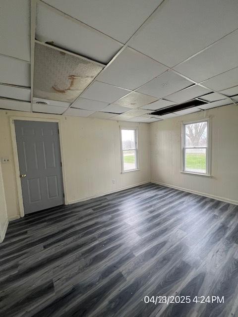 unfurnished room with dark wood finished floors, healthy amount of natural light, baseboards, and a paneled ceiling