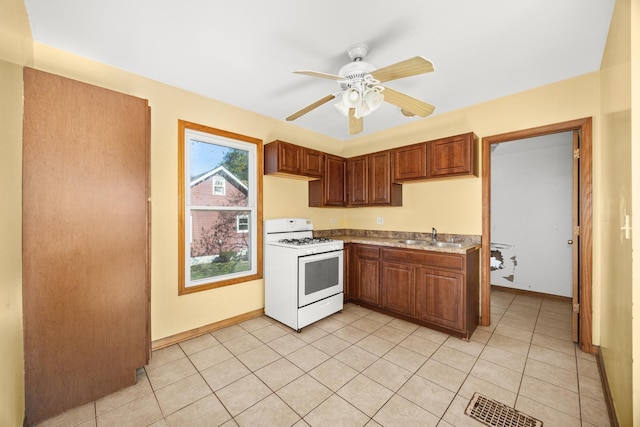 kitchen featuring white gas range oven, a sink, ceiling fan, and baseboards