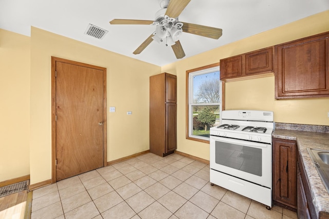 kitchen featuring white gas range oven, ceiling fan, baseboards, and brown cabinets