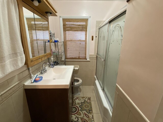 3846 Brummel St, Skokie, IL 60076 - bathroom featuring tile walls, tile patterned floors, toilet, vanity, and shower / bath combination with glass door