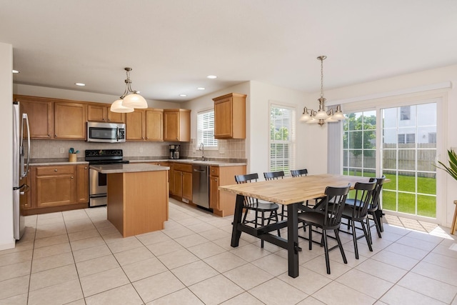 kitchen featuring appliances with stainless steel finishes, a kitchen island, light countertops, light tile patterned floors, and backsplash