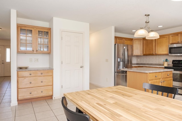 kitchen with appliances with stainless steel finishes, light tile patterned floors, light countertops, backsplash, and glass insert cabinets