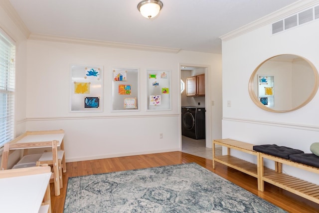 living area with ornamental molding, washing machine and dryer, wood finished floors, and baseboards