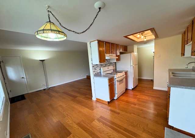 kitchen with white appliances, a sink, under cabinet range hood, and wood finished floors