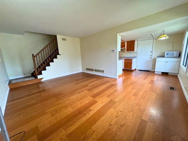 unfurnished living room featuring light wood-type flooring, stairway, and baseboards