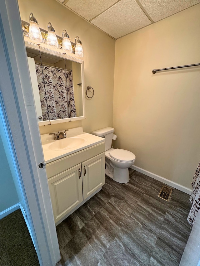 bathroom featuring toilet, vanity, a shower with shower curtain, and a drop ceiling