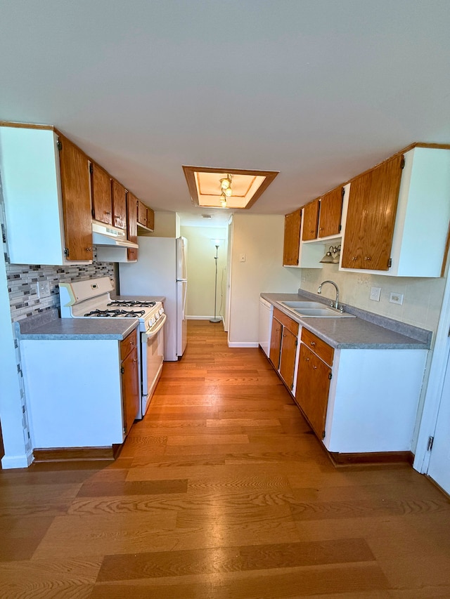 kitchen with white appliances, a sink, under cabinet range hood, light wood-style flooring, and tasteful backsplash