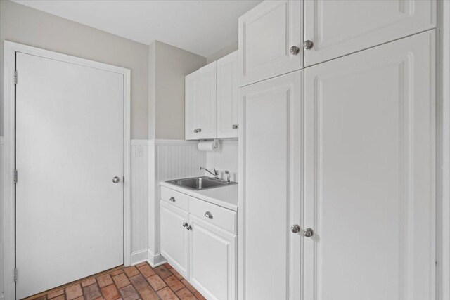 519 Long Hill Rd, Gurnee, IL 60031 - kitchen featuring a sink, brick patterned flooring, white cabinets, light countertops, and a wainscoted wall
