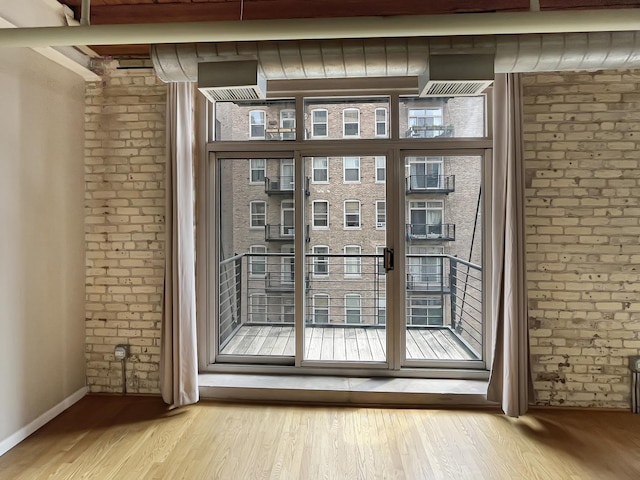 doorway to outside featuring wood finished floors, baseboards, and brick wall