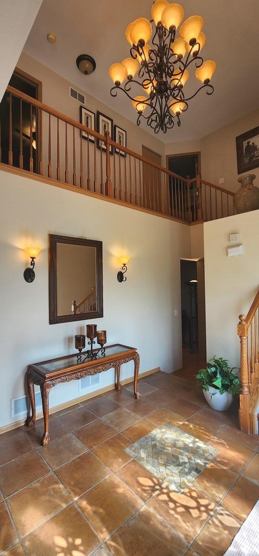 dining space with a high ceiling, a chandelier, baseboards, stairs, and stone finish flooring