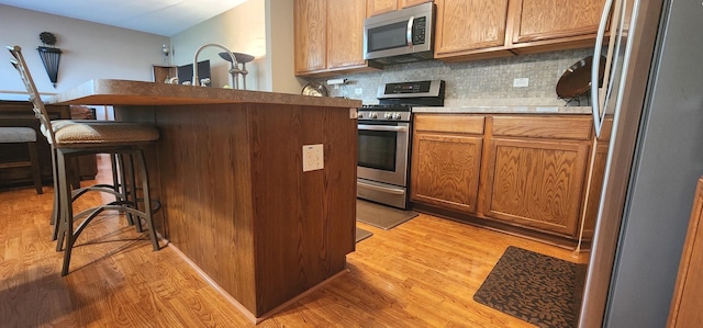 kitchen featuring stainless steel appliances, light wood-style flooring, a kitchen bar, and tasteful backsplash