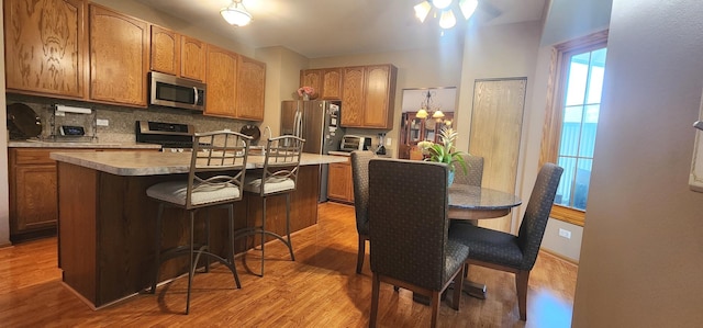 kitchen featuring appliances with stainless steel finishes, light wood finished floors, decorative backsplash, a breakfast bar area, and a kitchen island
