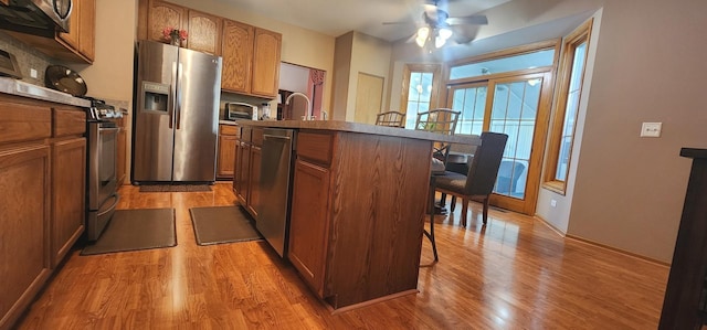 kitchen featuring appliances with stainless steel finishes, a breakfast bar area, light wood-type flooring, a ceiling fan, and a center island with sink