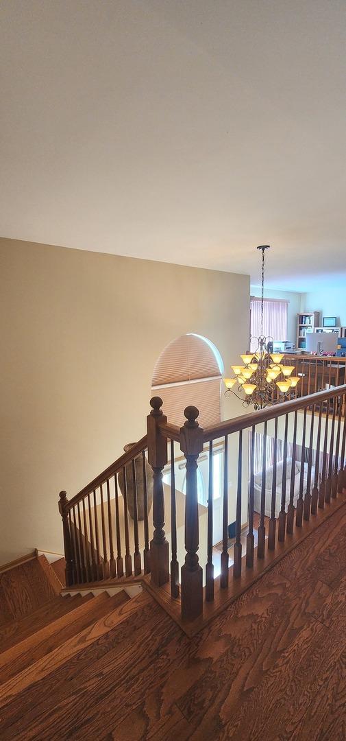 stairway with wood finished floors and a chandelier