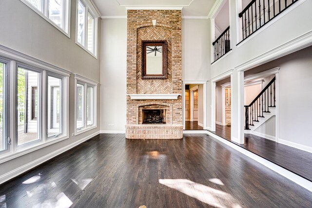 1565 Winberie Ct, Naperville, IL 60564 - unfurnished living room with plenty of natural light, a brick fireplace, a towering ceiling, dark wood-style flooring, and crown molding