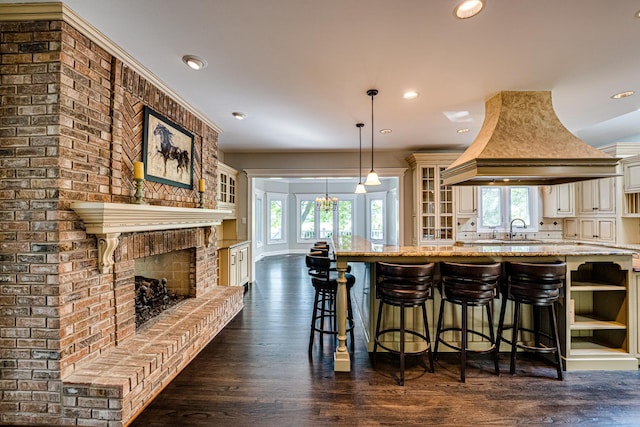 1565 Winberie Ct, Naperville, IL 60564 - kitchen with glass insert cabinets, light stone counters, premium range hood, a brick fireplace, and recessed lighting