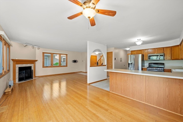 11046 Quail Dr, Mokena, IL 60448 - kitchen with appliances with stainless steel finishes, light countertops, a tiled fireplace, light wood finished floors, and a peninsula