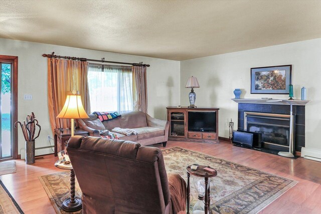 7 Birch Ln, Villa Grove, IL 61956 - living room featuring wood finished floors, a tile fireplace, a textured ceiling, and baseboard heating